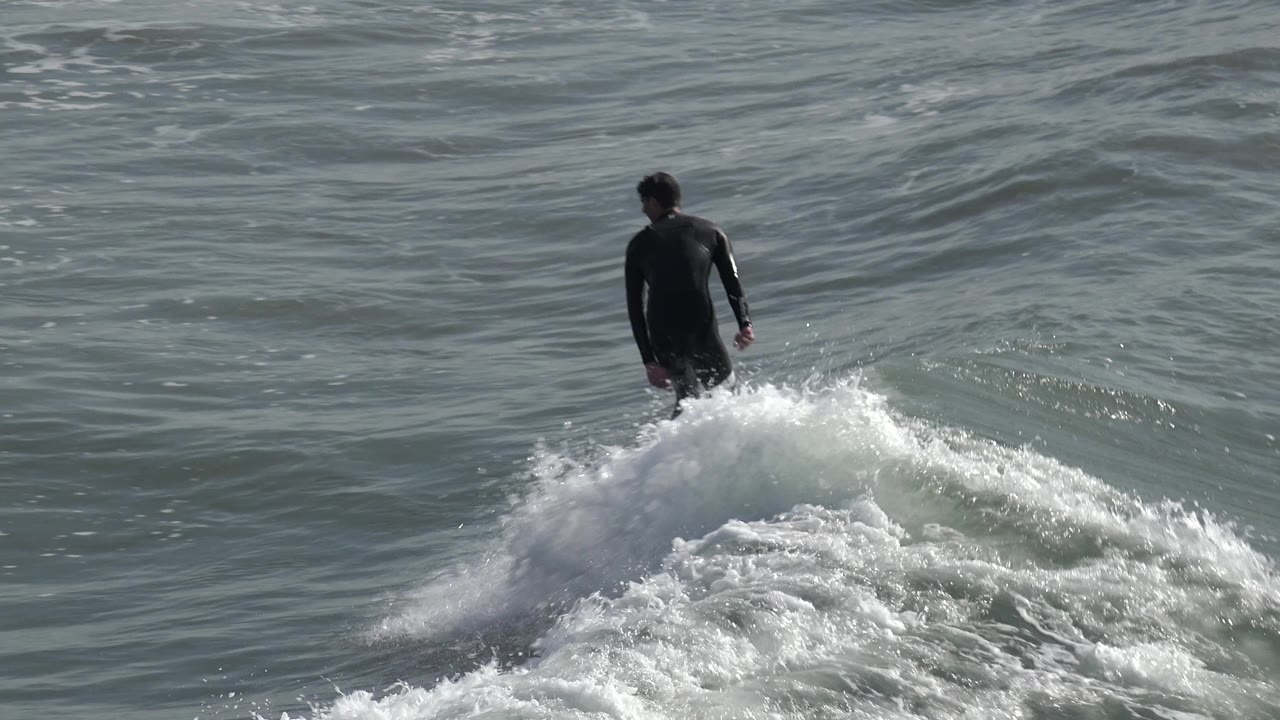 Surfer stands near the top of a breaking wave with foam below.