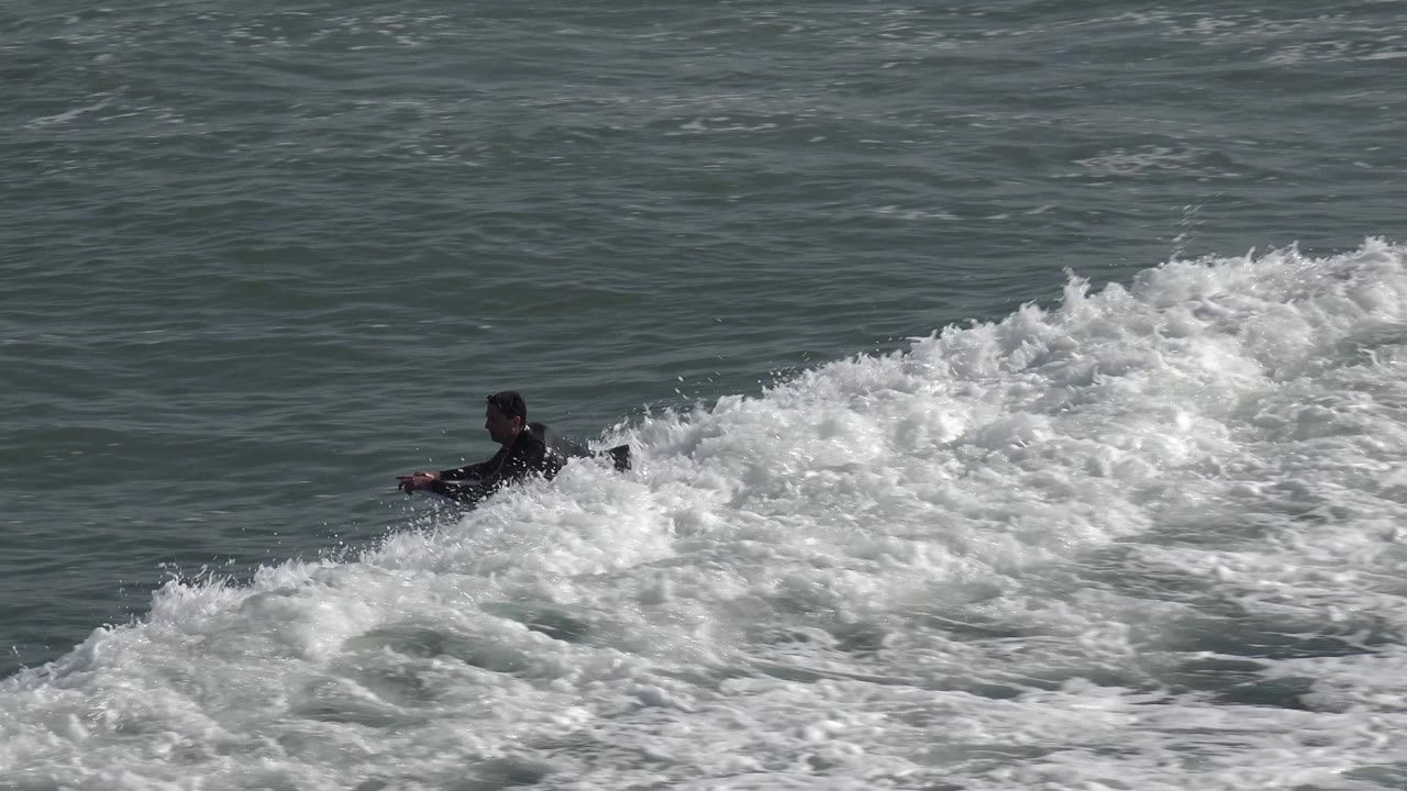 Surfer sits low on a board in foamy water.