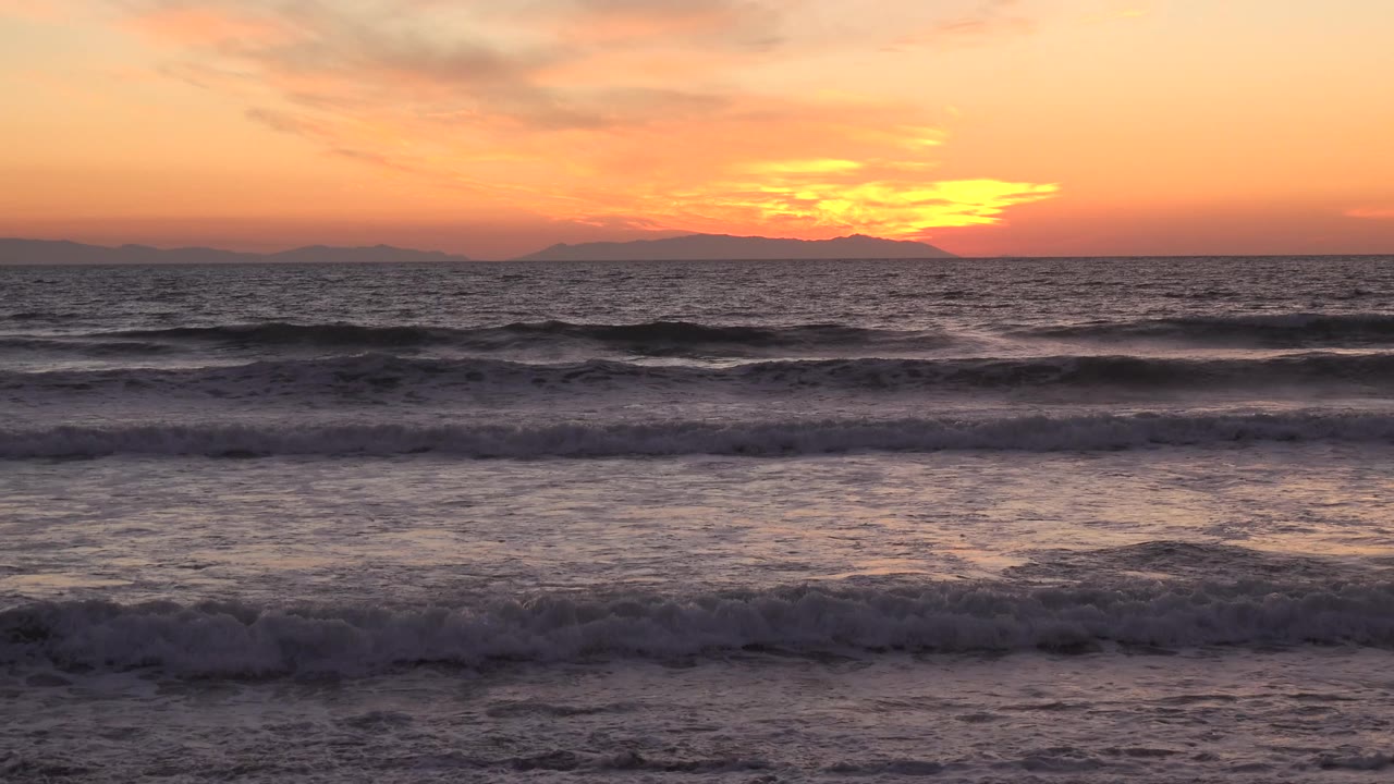 Huntington Beach surf forms layered dark wave bands beneath a brighter orange glow near the horizon, with no visible people in frame.