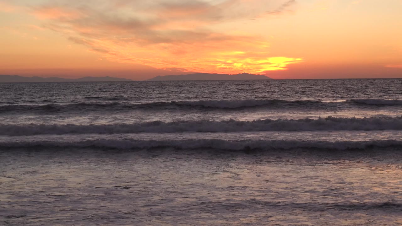 Huntington Beach, California ocean at sunset with orange cloud light above layered surf and no visible people.