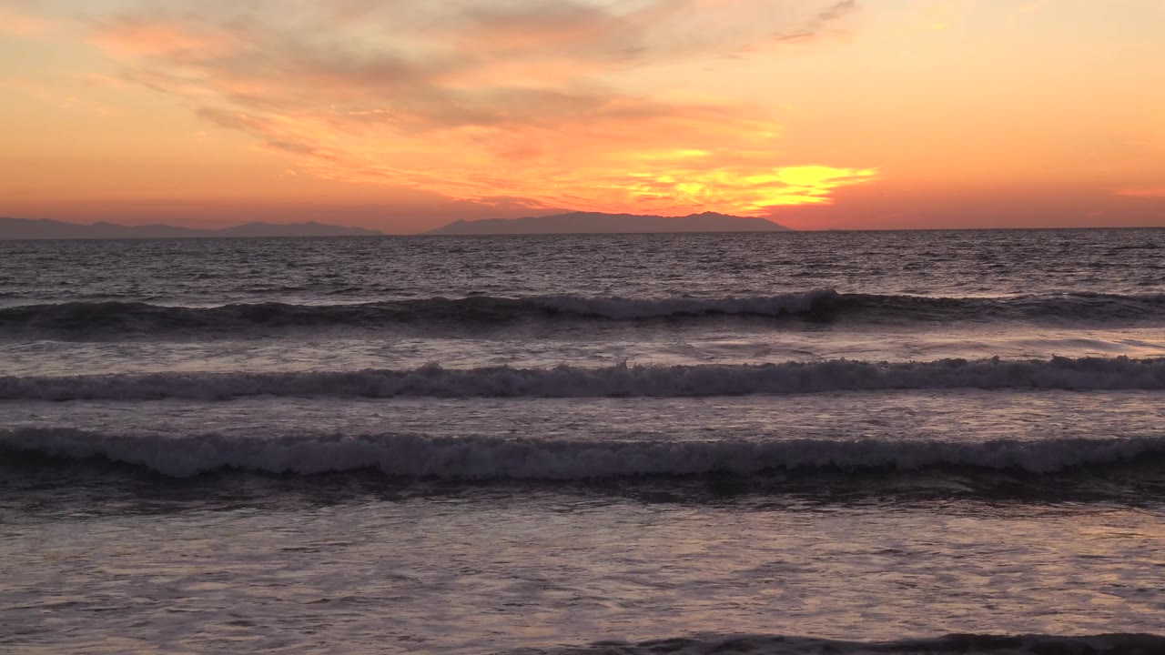 Huntington Beach, California shoreline water at dusk with a broad orange sky, breaking surf, and no visible people.