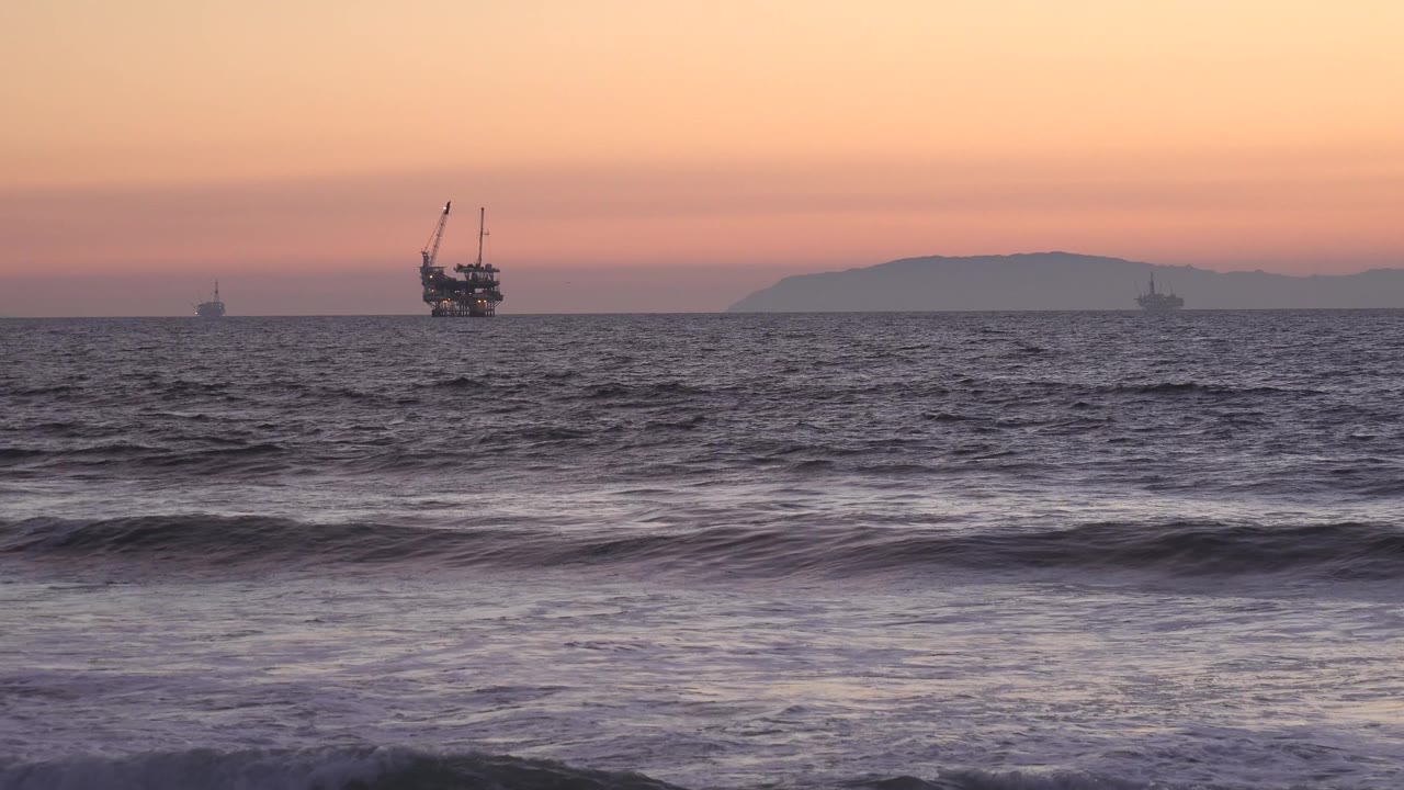 At Huntington Beach, a larger offshore vessel remains left of center with smaller silhouettes near the horizon and choppy water in the foreground, with no visible people.