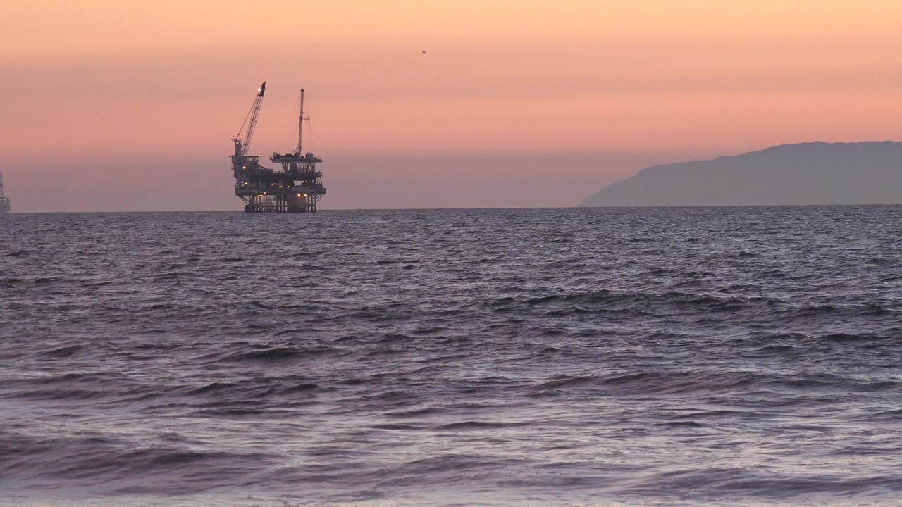 Distant offshore platform over ocean waves at sunset.