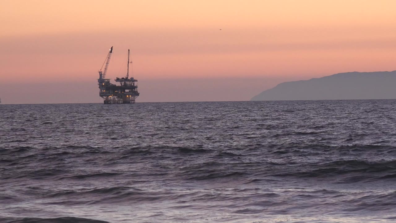 Offshore industrial platform on a sunset ocean horizon with waves in front.