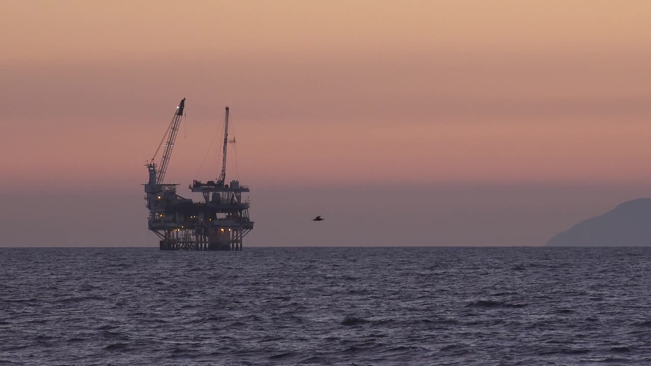 Bird flying low over the water beside an offshore platform.