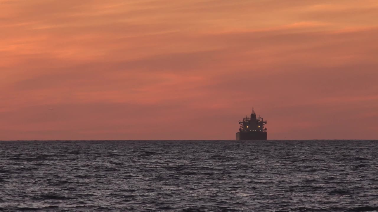 Tanker on the horizon beneath a warm orange sky.