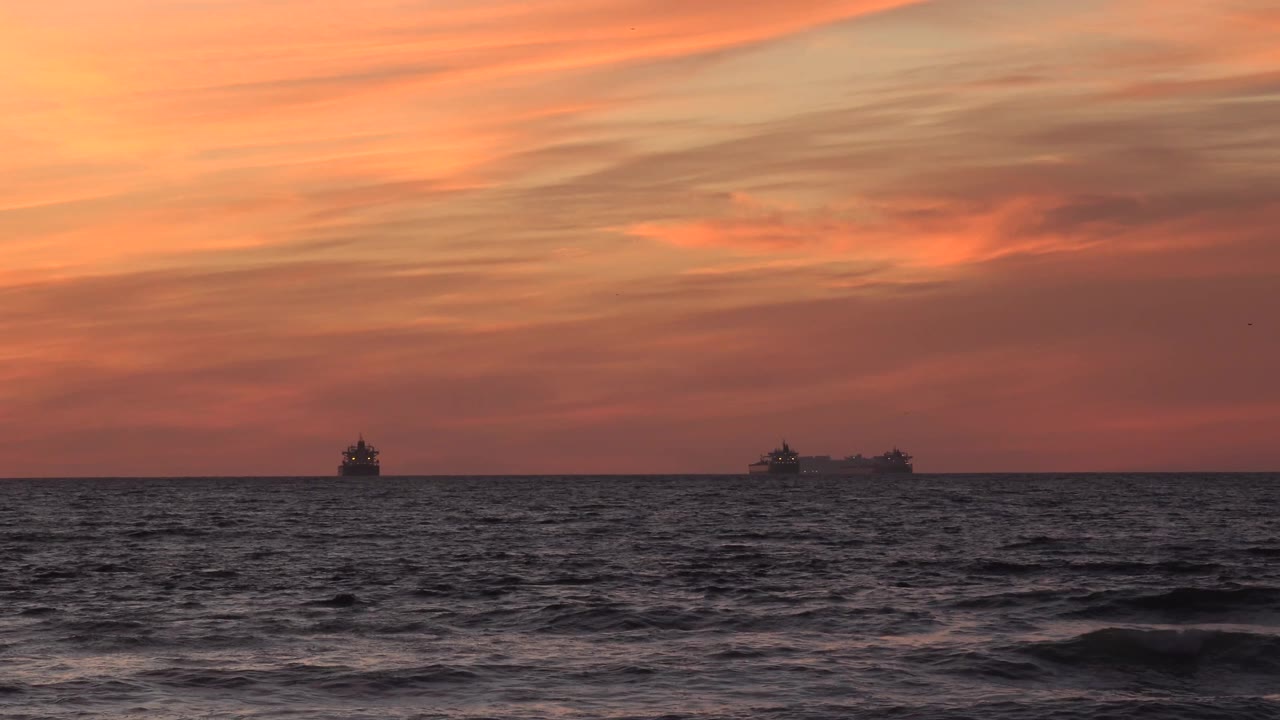 Huntington Beach ocean horizon with a small ship left of center, larger ship shapes to the right, dark textured water, and no visible people.