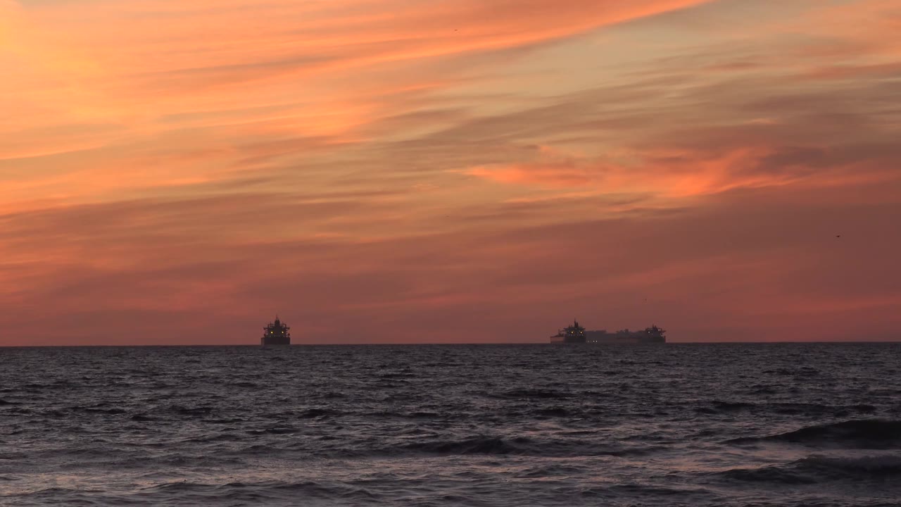 Huntington Beach sunset view with choppy foreground water, a low straight horizon, ship silhouettes spread across the background, and no visible people.
