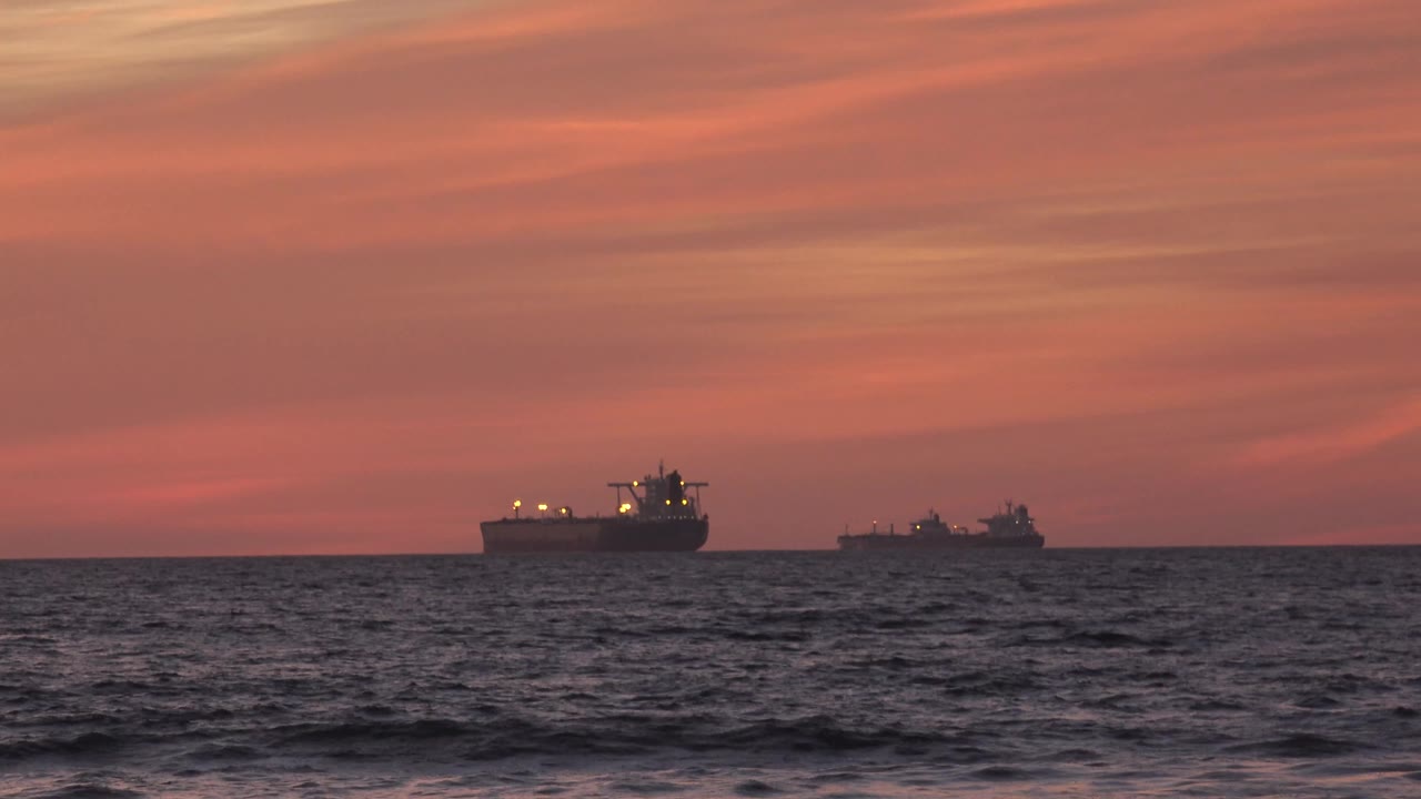 Two distant cargo ships on the ocean horizon at sunset.