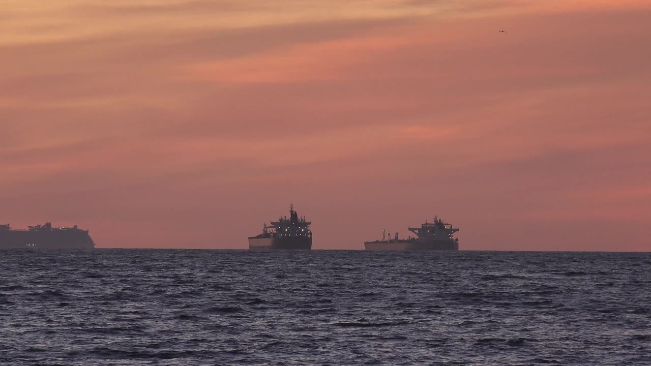 Barges silhouetted offshore with dark water below.