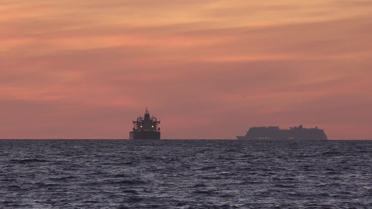 Two distant ships silhouetted on a red ocean horizon.