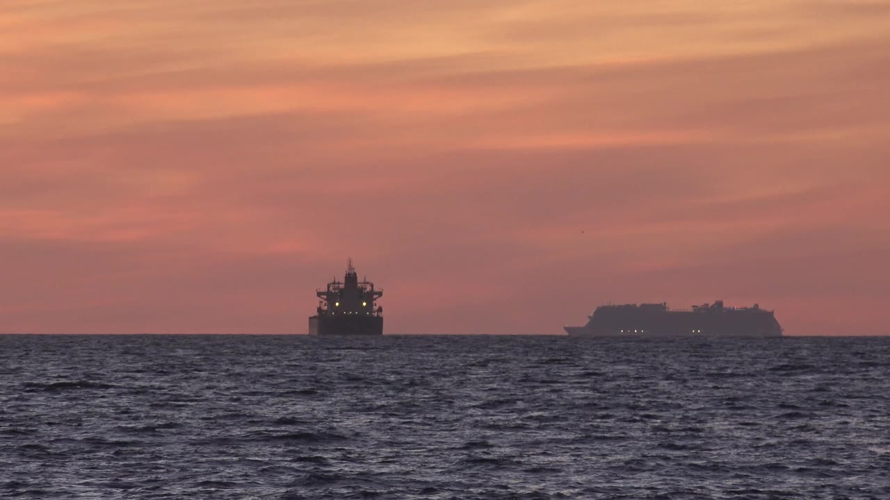 At Huntington Beach, the dark ocean texture shifts below two distant vessels on the horizon, with soft red cloud bands above and no visible people.