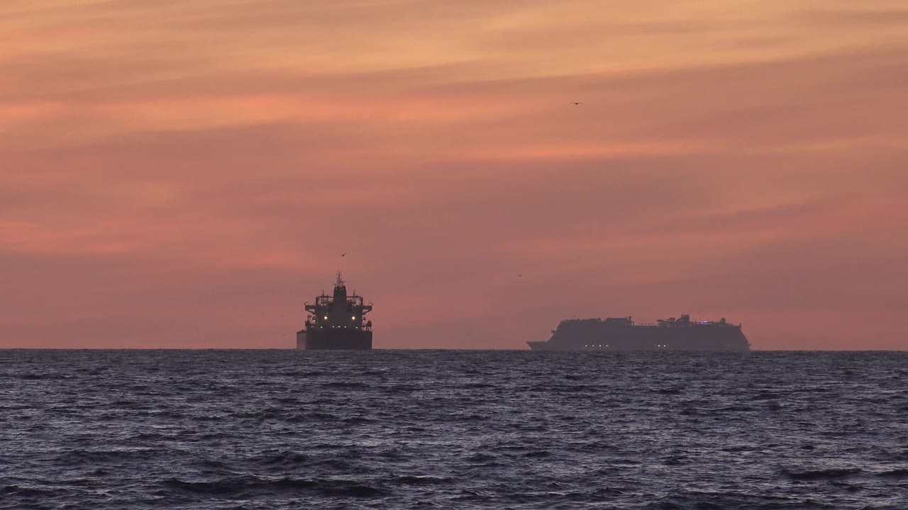 Sunset ocean horizon with two dark vessels and rippled water.