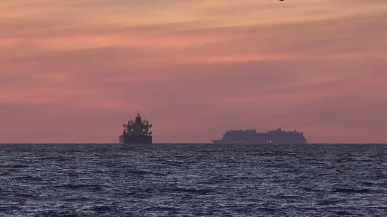 Distant ships and rippled ocean water beneath a warm sunset sky.