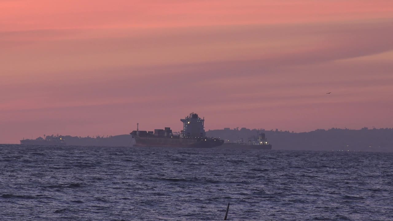 Ship sits slightly right of center off Huntington Beach, California, with choppy foreground water, muted land behind it, and no visible people.