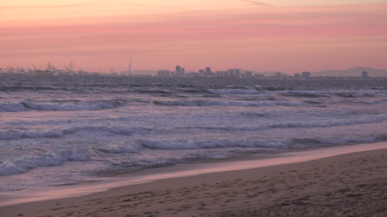 Huntington Beach surf fills more of the frame as foam spreads over the water, with a sandy strip in front, a hazy distant coast, and no visible people.