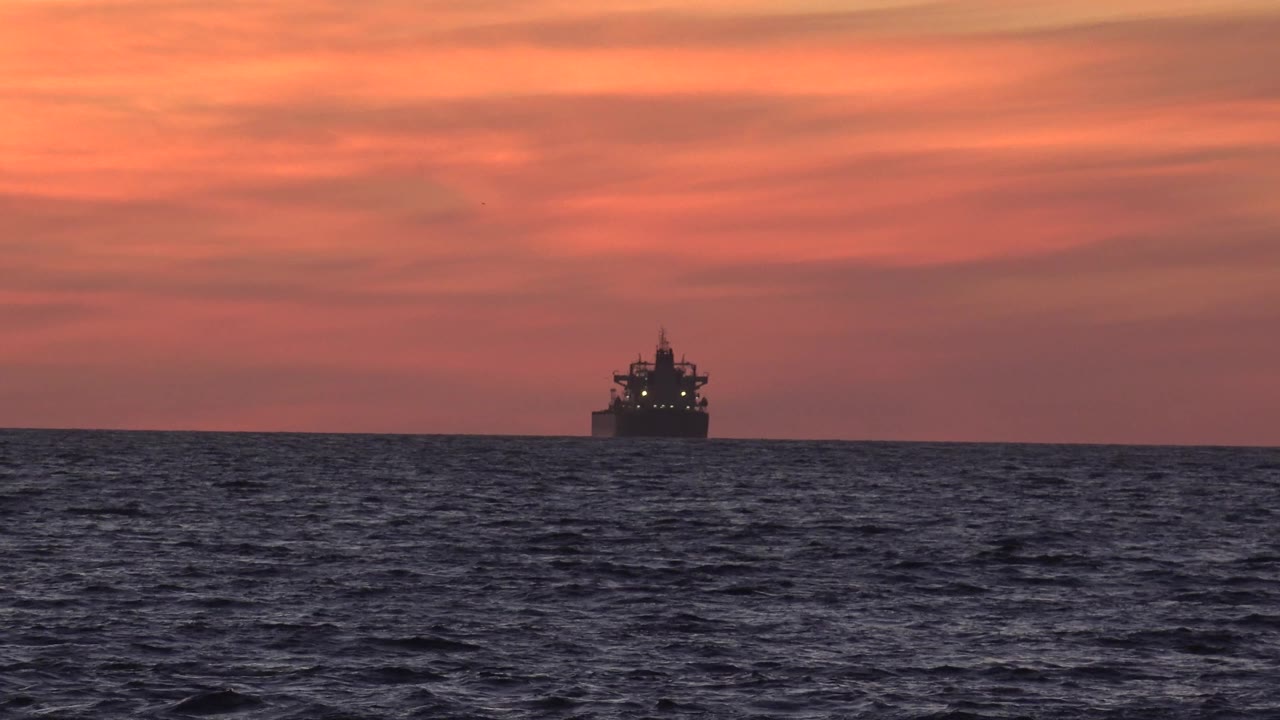 Large boat silhouette beyond dark ocean waves at dusk.