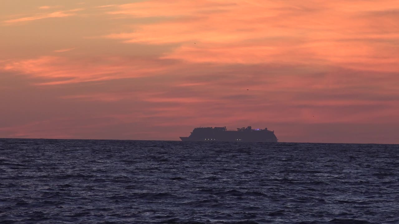 A ship silhouette sits farther right on the Huntington Beach ocean horizon under streaked pink-orange clouds, with no visible people in frame.