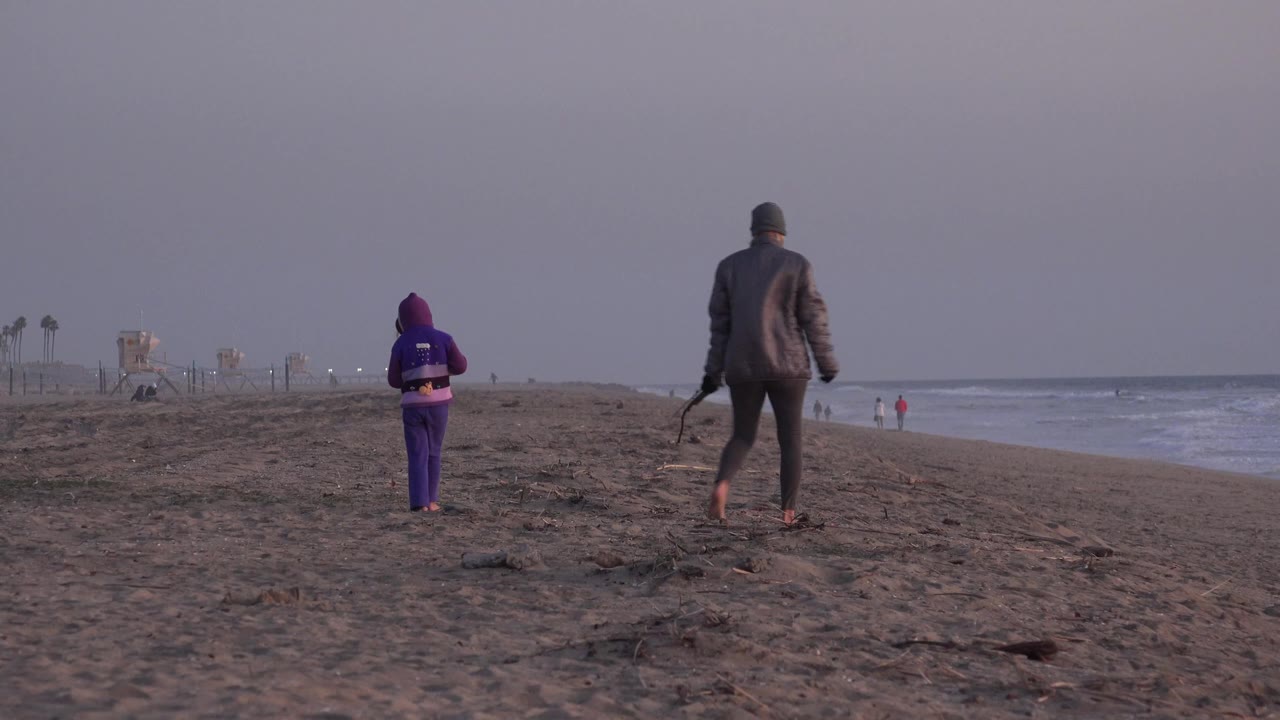 Adult and child continue along the sand beside the surf