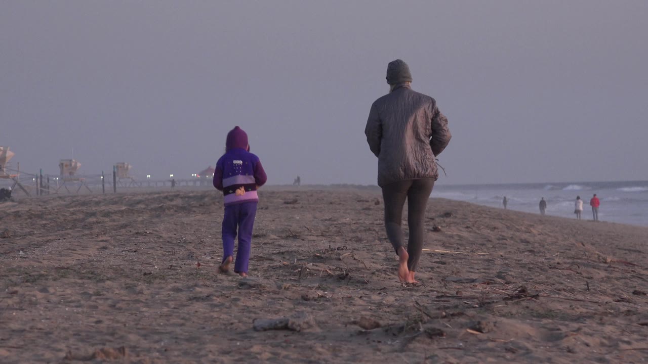 Two barefoot walkers move along the sand with beach towers in the background.