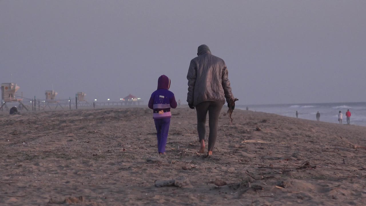 Adult and child continue down the sandy shoreline.