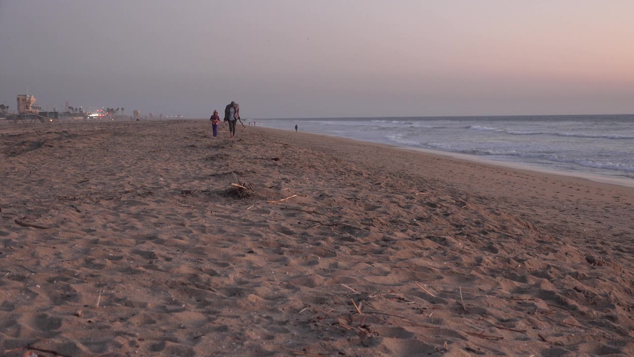 Two people walking toward the camera on a quiet sunset beach.