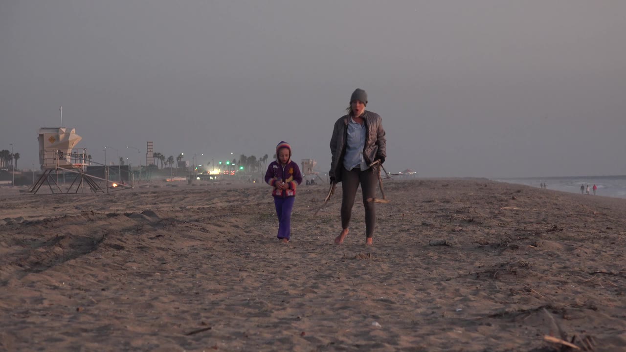 Man and child walking closer on beach at dusk