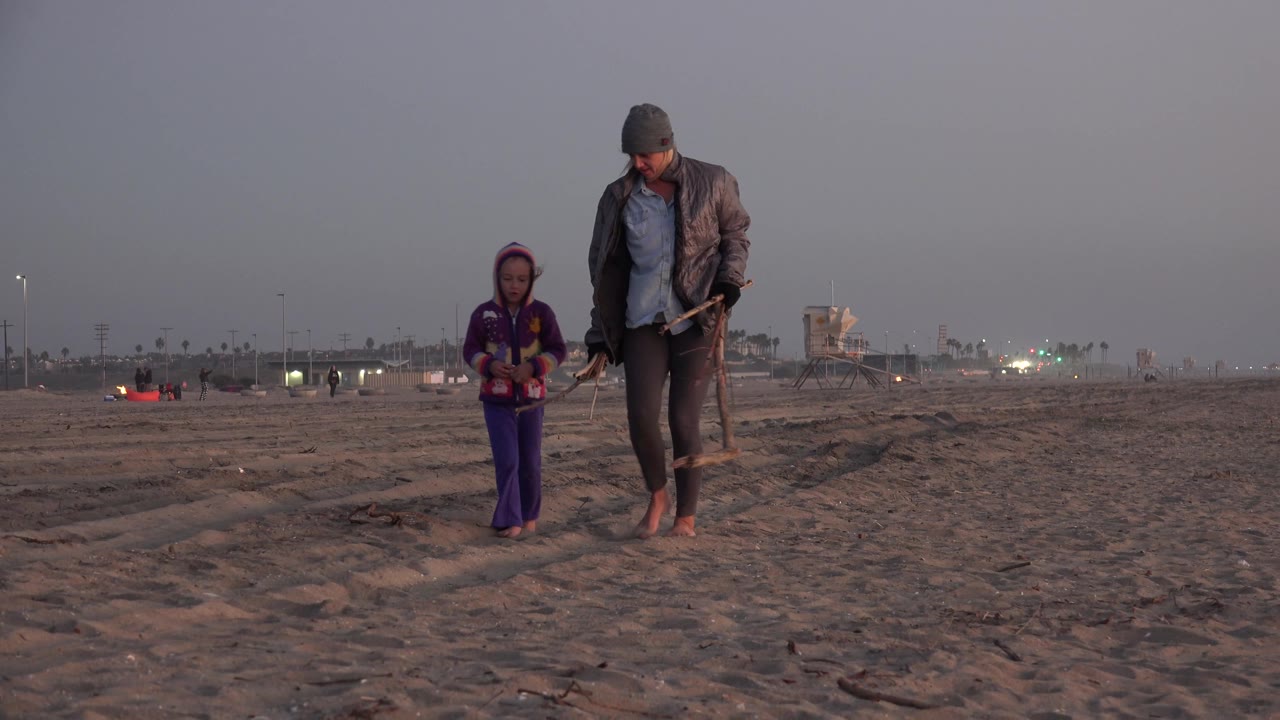 Child and adult walking toward the camera on sand.