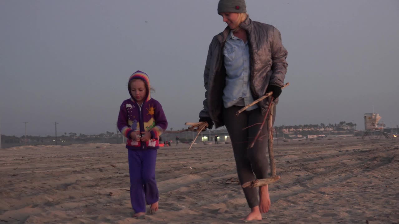 Young girl and mother continue walking across beach sand.