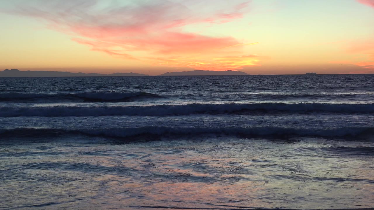 Sunset waves rolling toward a dark beach horizon