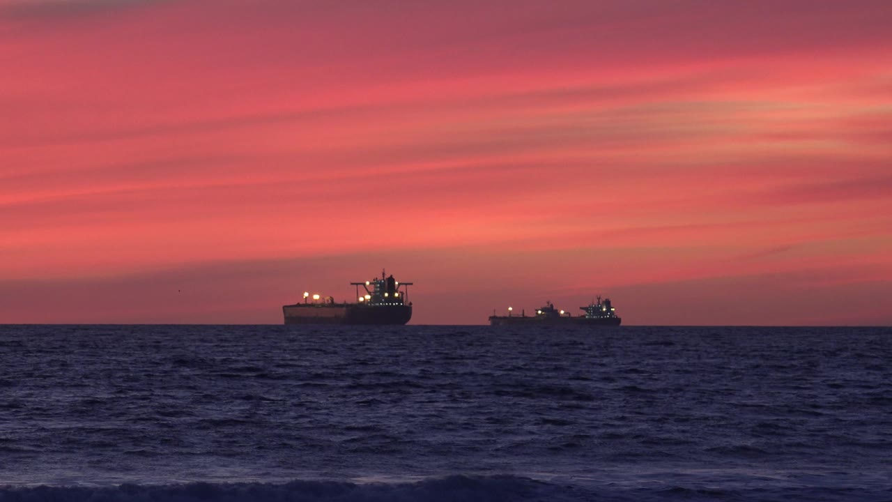 Two ships on the ocean horizon under a red sunset sky.