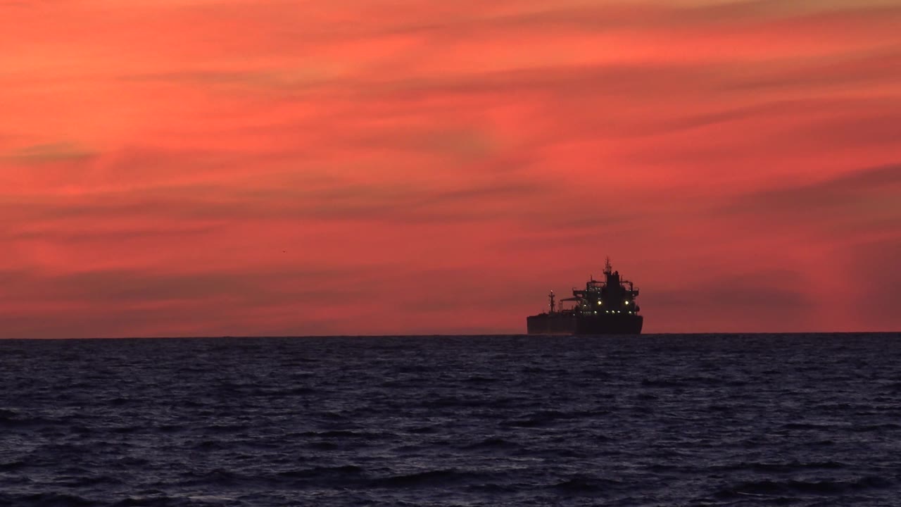 Dark ship silhouette on the horizon with rolling ocean in the foreground.