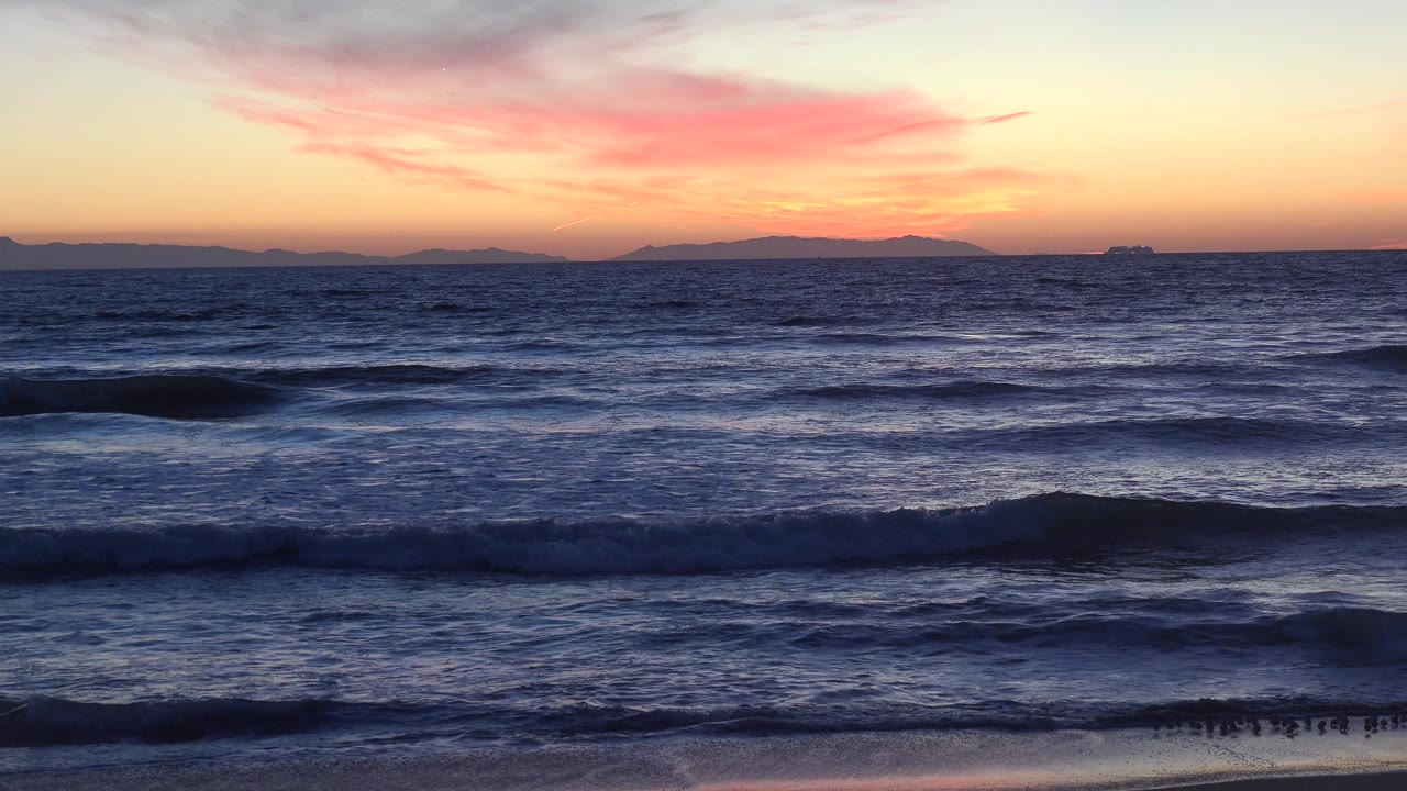 Sunset ocean waves with wet beach and distant horizon.
