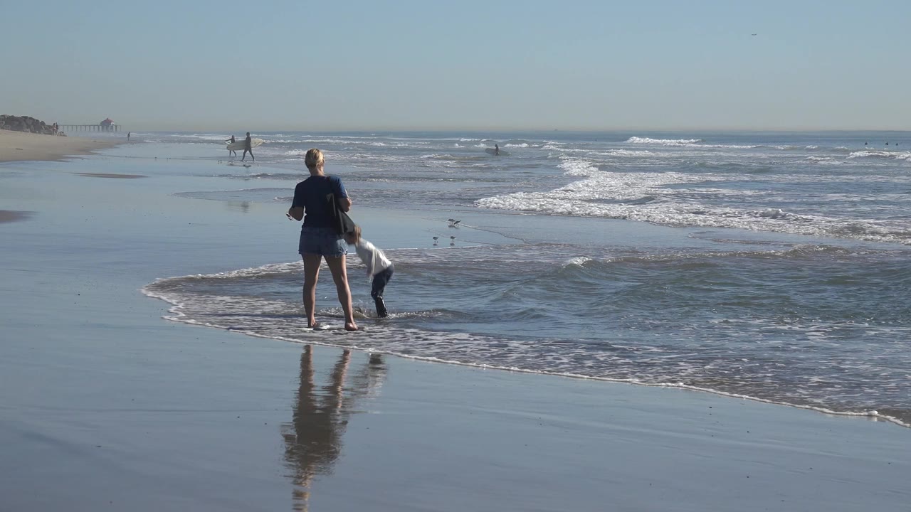 Adult facing the surf while a child bends near the water.