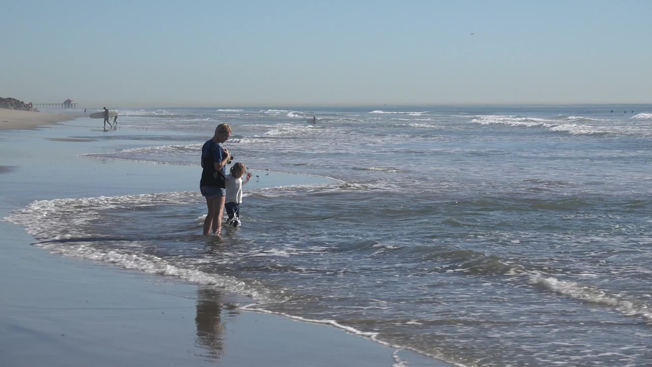 Woman watching child at the edge of a small wave.