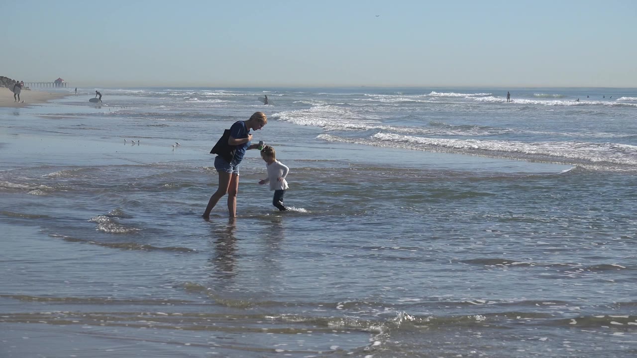 Adult and child stand together as waves spread across wet sand.