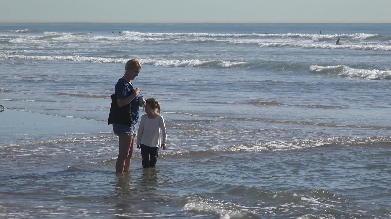At Huntington Beach, California, the grandmother and child remain in the midground as a thin wave line spreads across the shallow water.