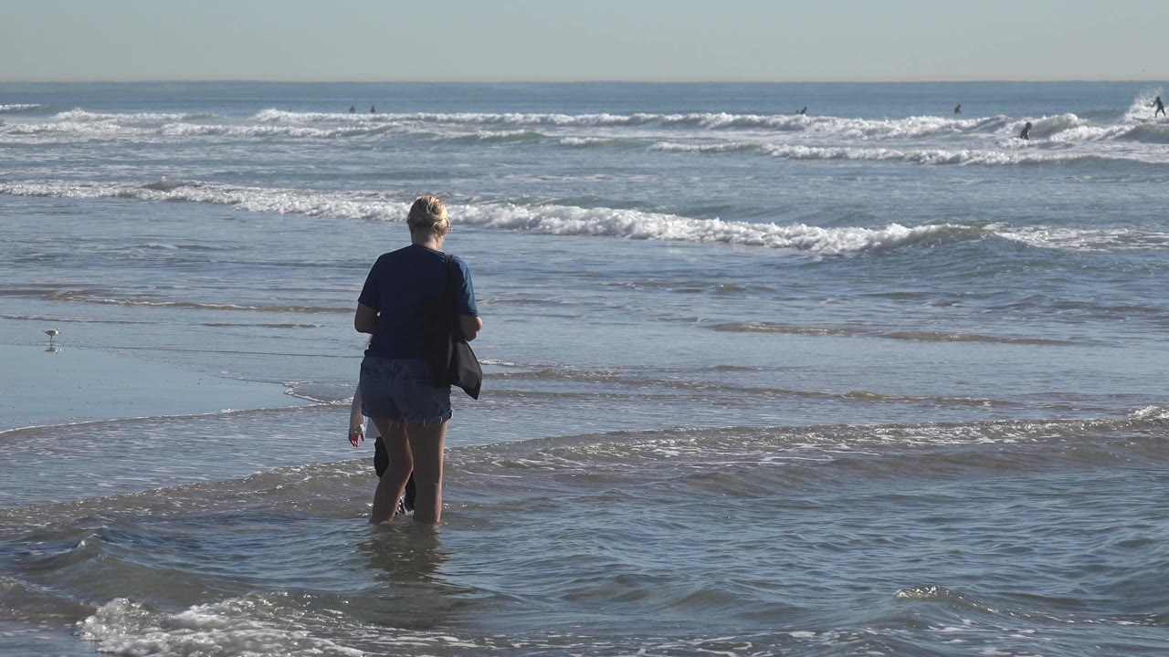 Grandmother and child seen from behind at the shoreline.