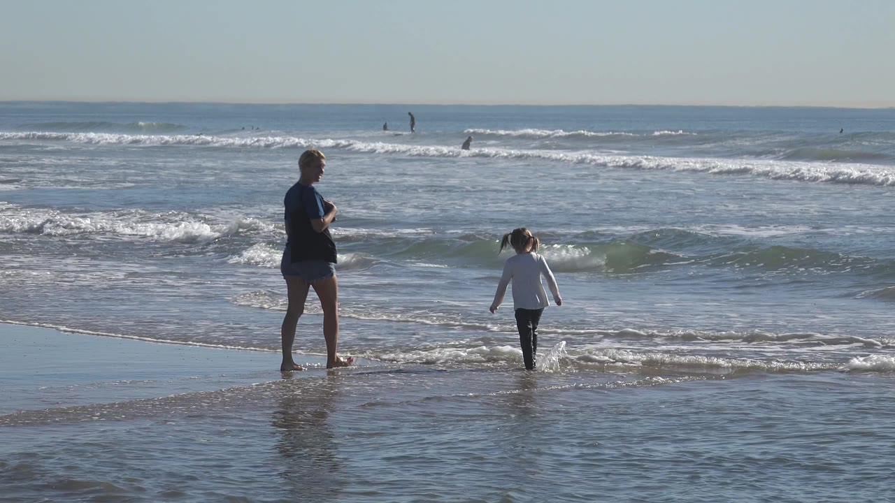 Woman stands as a child moves through a small wave.