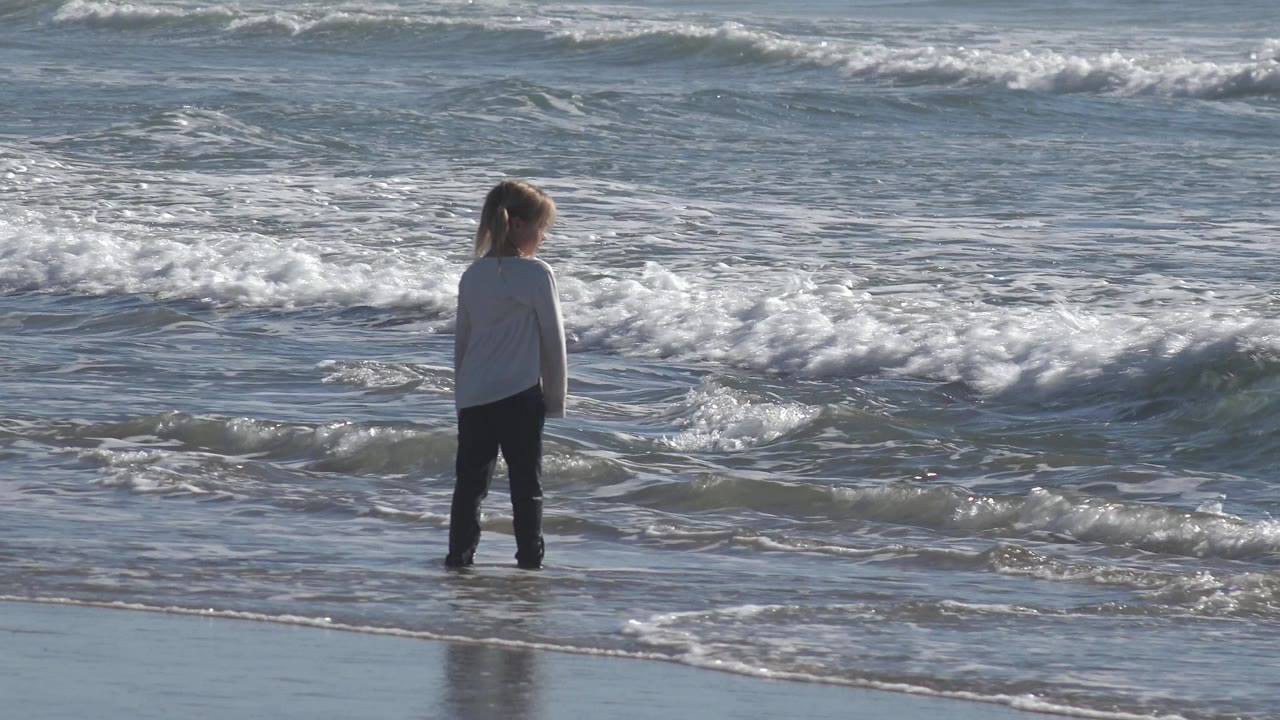 Child looking down near a breaking wave.