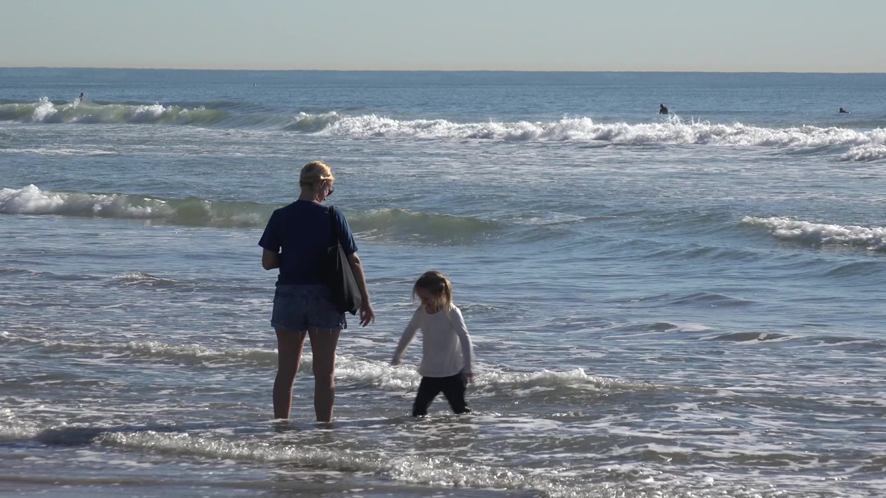 Woman and child near the waterline with broad surf in the background.