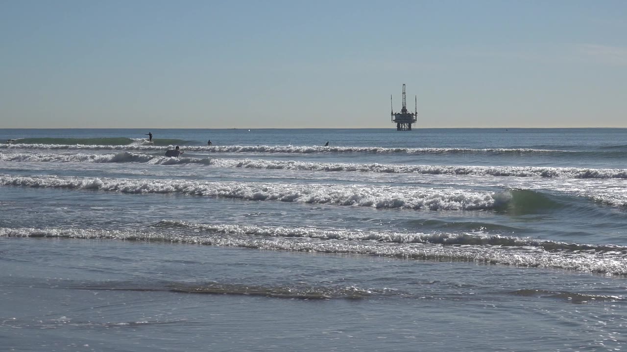 Rolling surf with an offshore oil rig on the horizon.