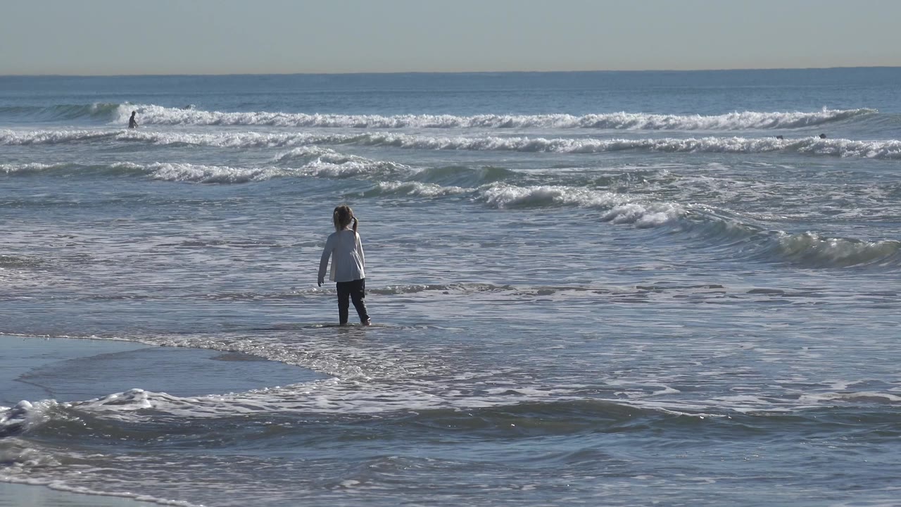 Girl facing the waves in shallow water on a sunny beach.