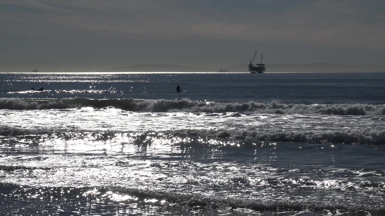 Bright ocean glare over rolling surf and a distant horizon structure