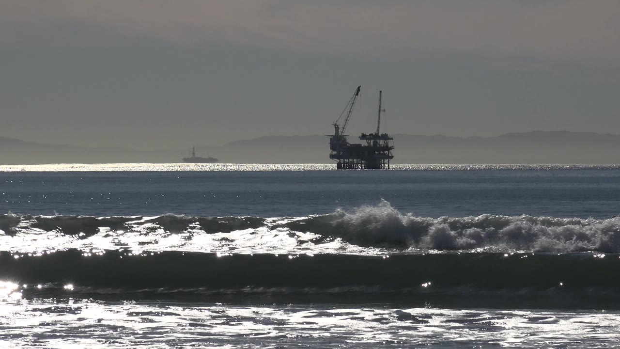 Offshore platform beyond rough surf and a bright strip of water.