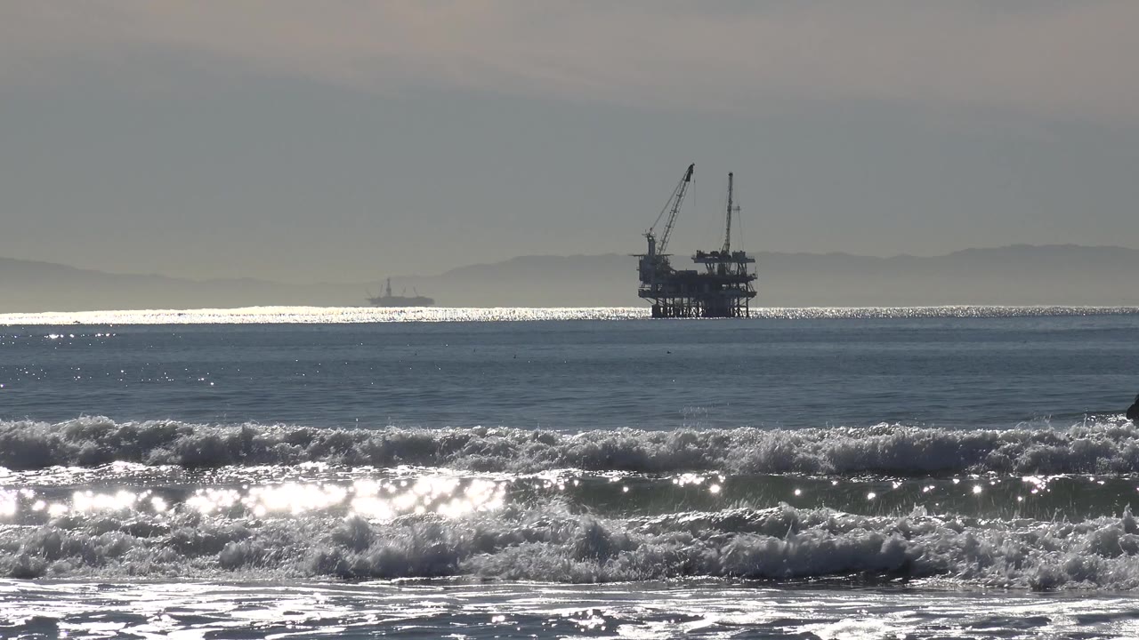 Oil rig on the horizon behind choppy surf and water glare.
