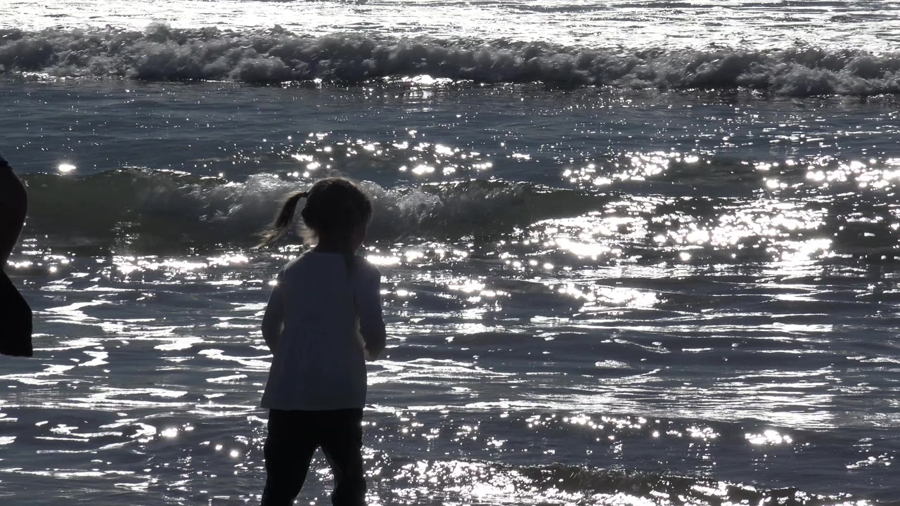 Child at the waterline with an adult silhouette nearby.