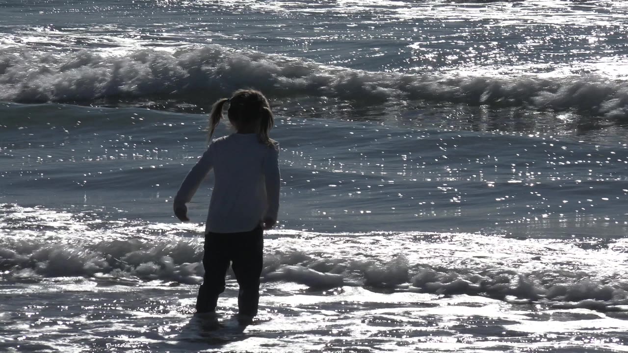 Child standing near foamy shoreline water.