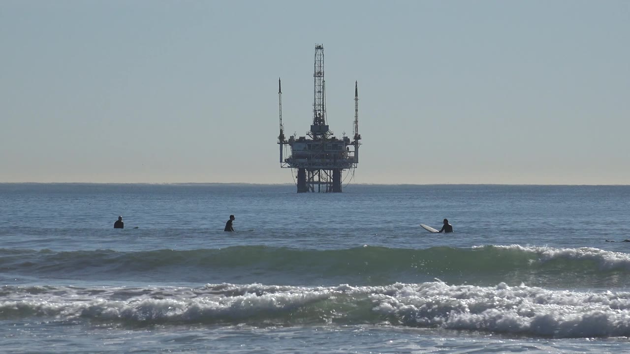 Distant surfers sit in the lineup as a wave begins to break near shore.