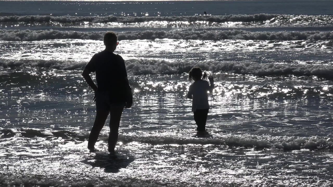 Adult watches child near foamy beach waves